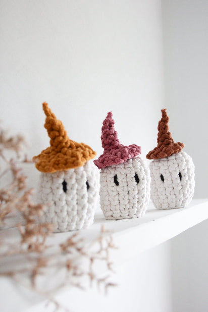Three crochet pumpkins with colorful hats on a white surface.