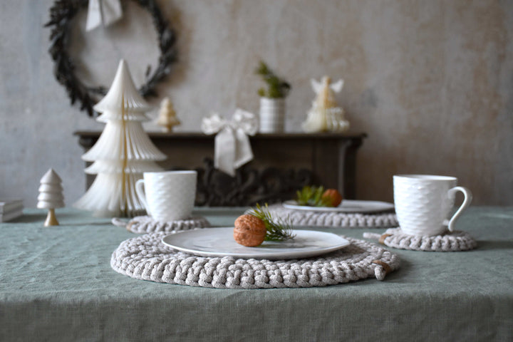 Table setting with white teacups, decorative trees, and a wreath in the background.