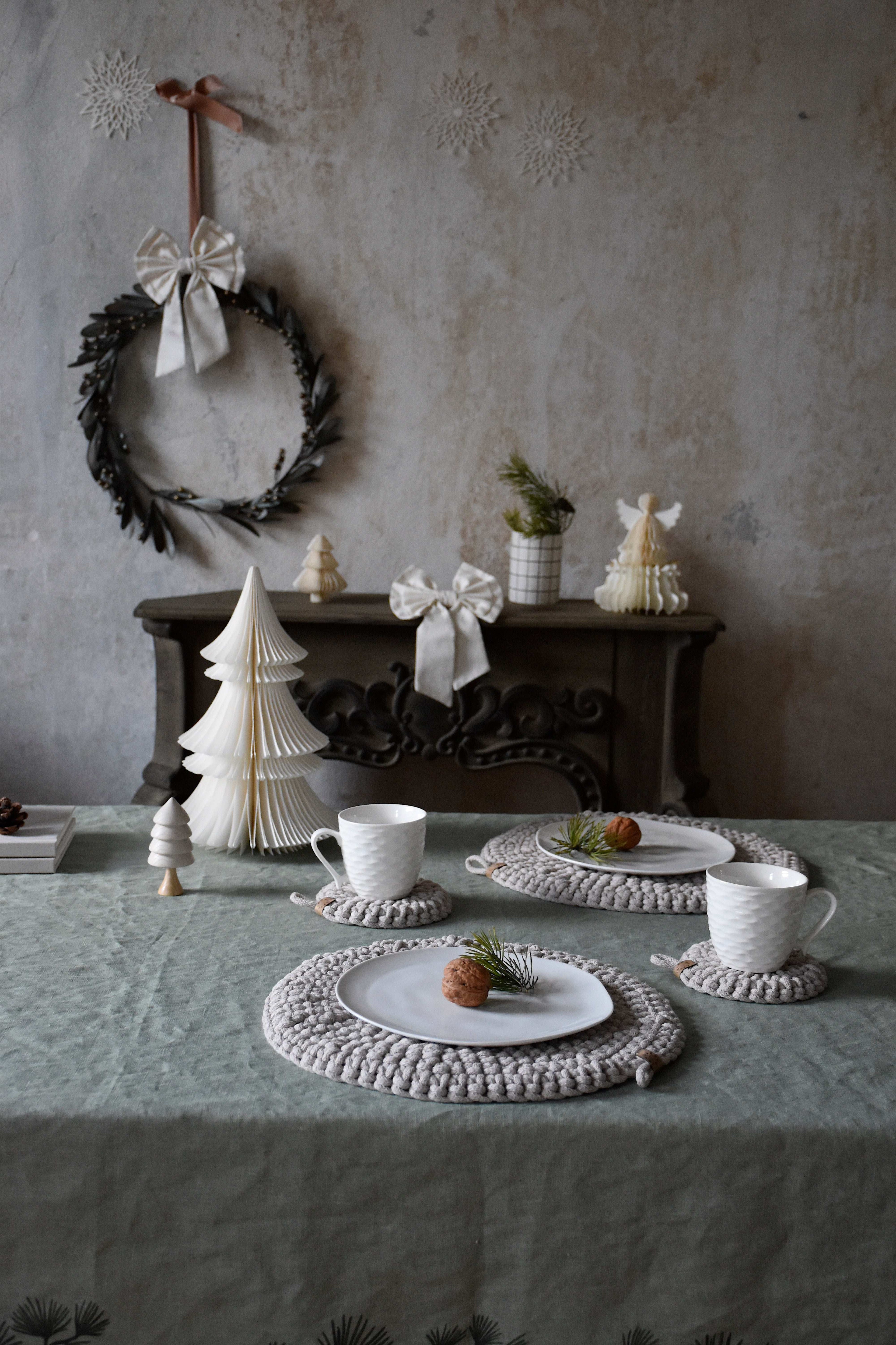 Dining table setting with crocheted placemats, teacups, and decorative items against a textured wall.