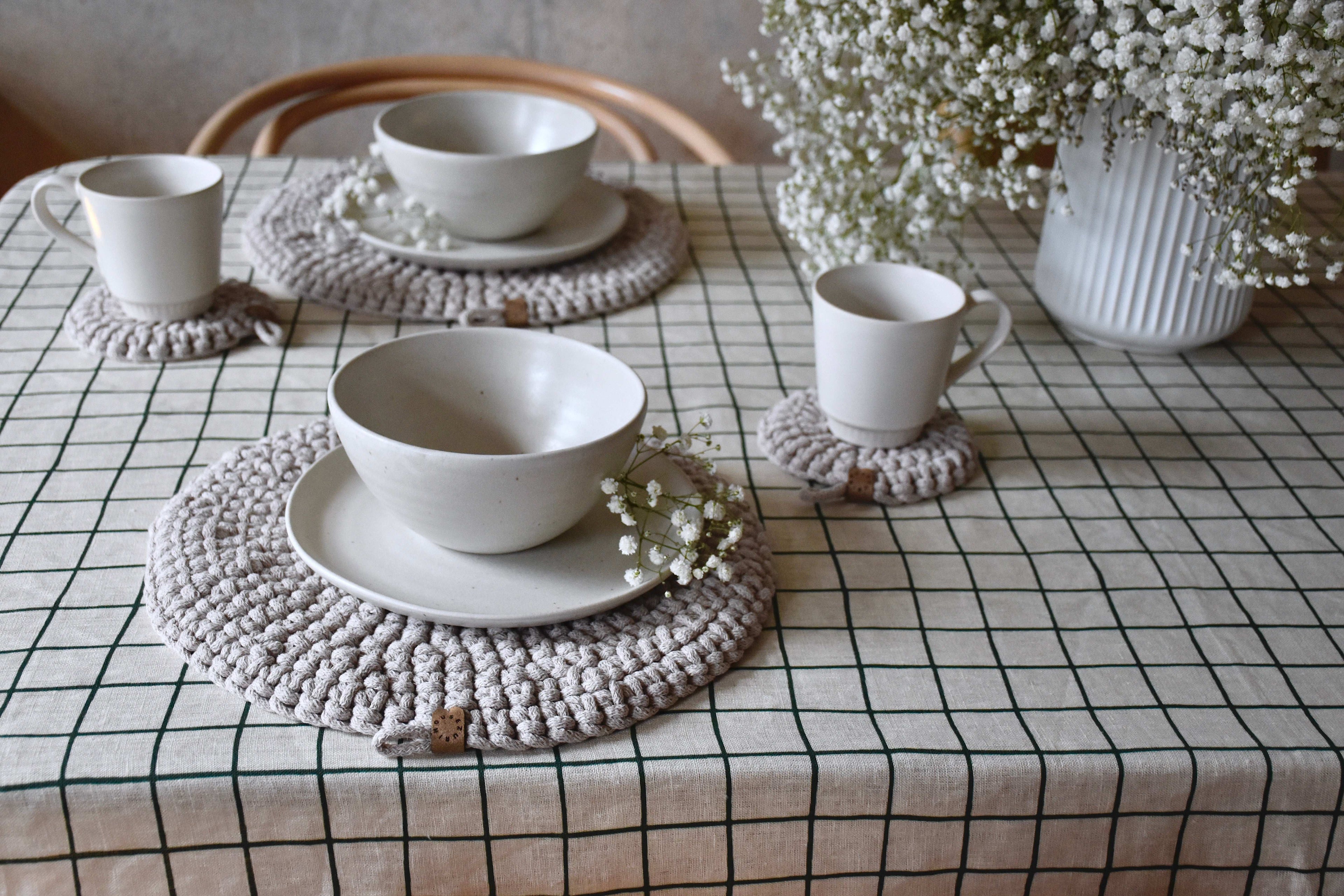 White ceramic bowls and cups on textured placemats with a checkered tablecloth and decorative elements.