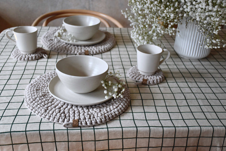White ceramic bowls and cups on textured placemats with a checkered tablecloth and decorative elements.