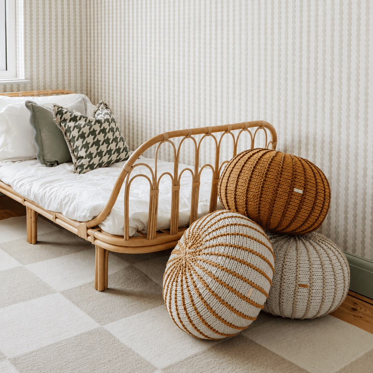 Three handmade Ziggy pouffes in striped neutral and caramel colourways beside a rattan daybed