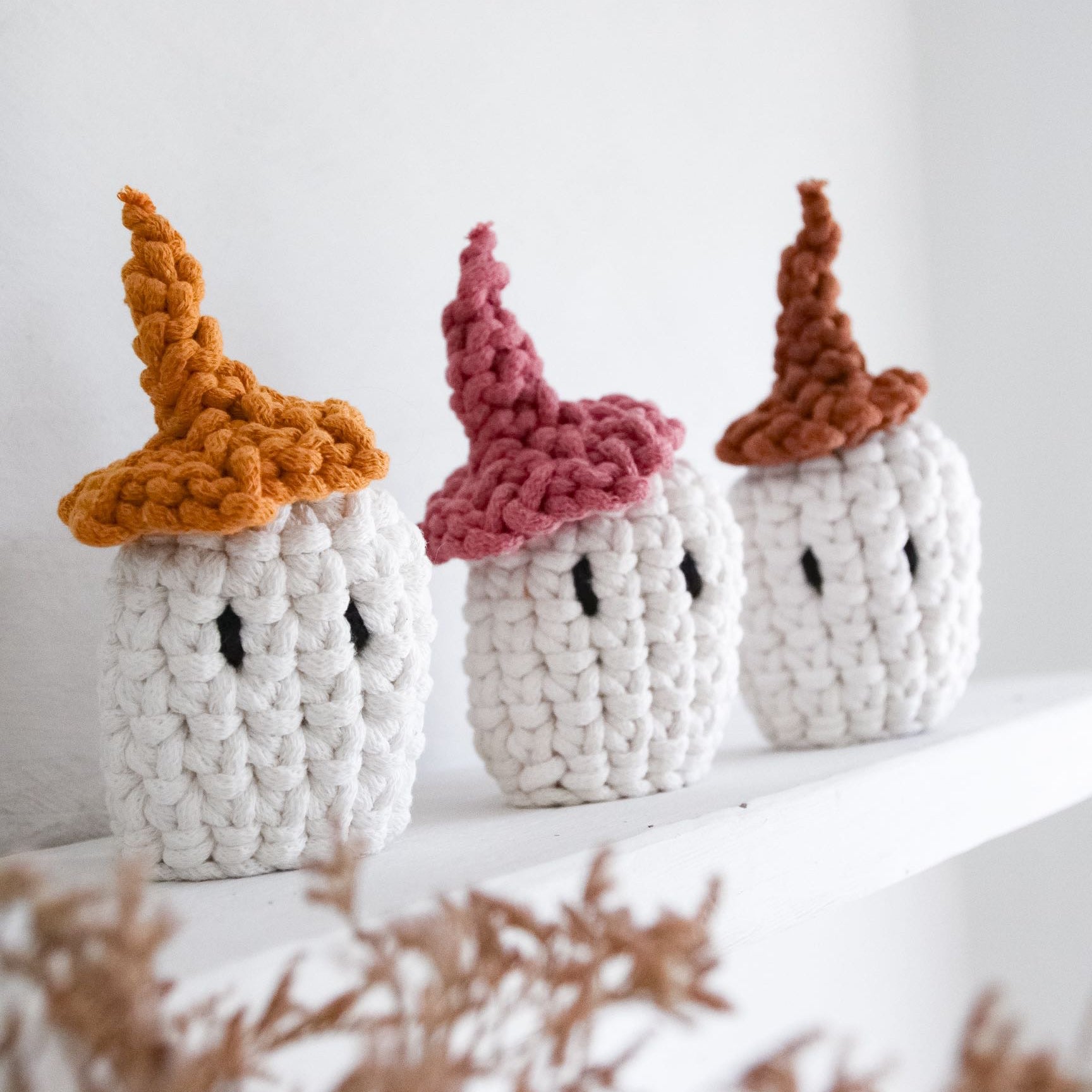 Three knitted pumpkins with colorful hats on a white surface.
