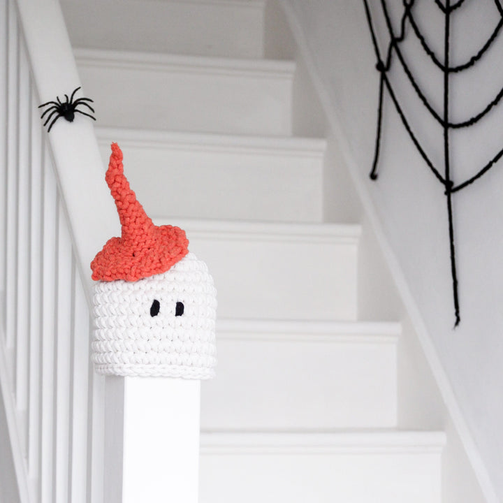 Crocheted ghost with a red hat on a staircase with Halloween decorations.