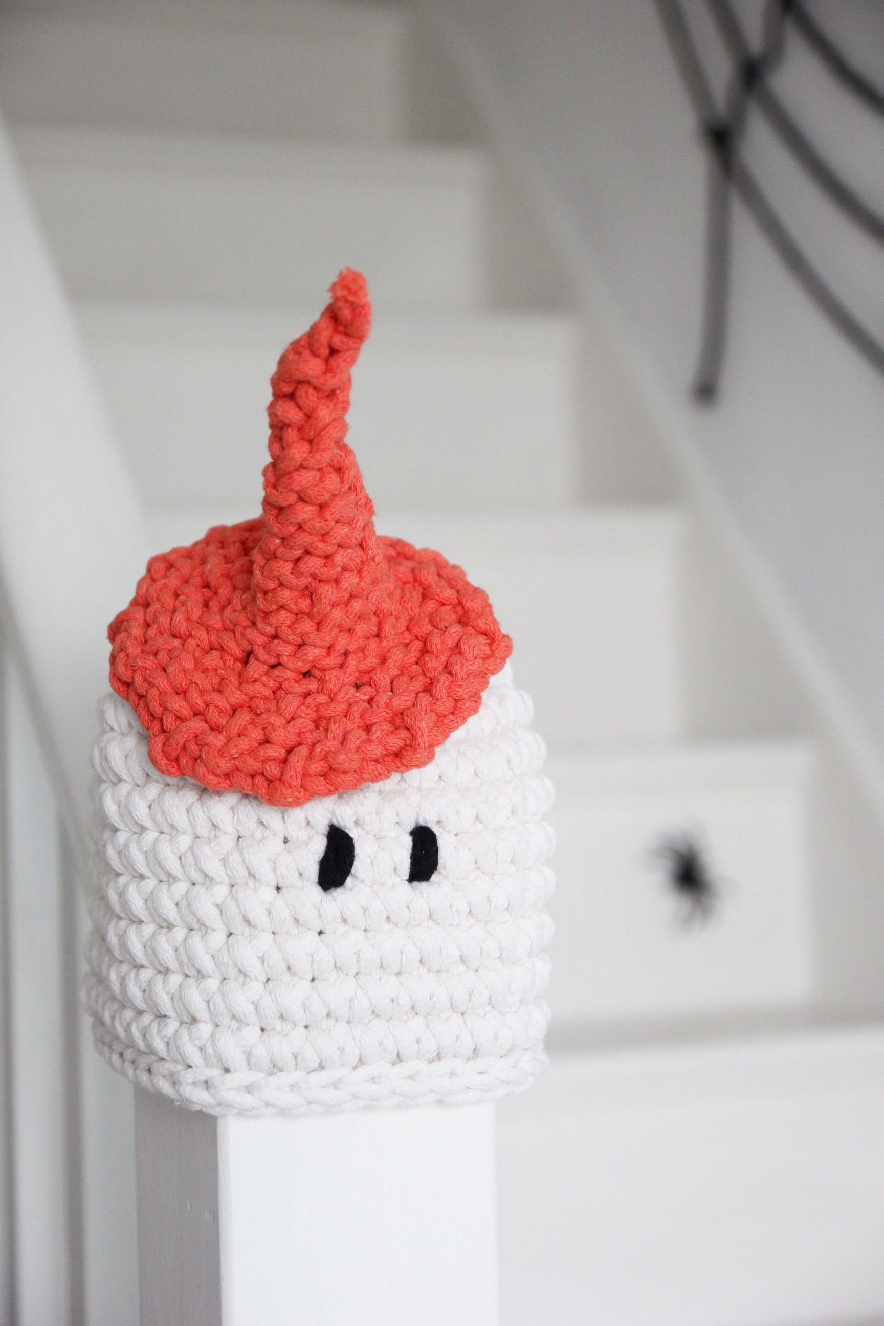 Crocheted character with a red hat and white body on a staircase background