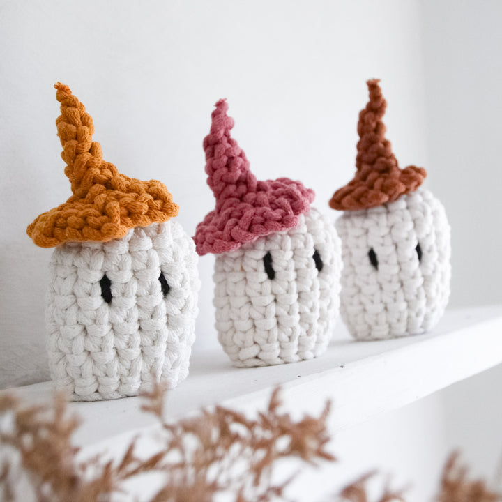 Three cute knitted ghosts with colorful tops on a white surface.