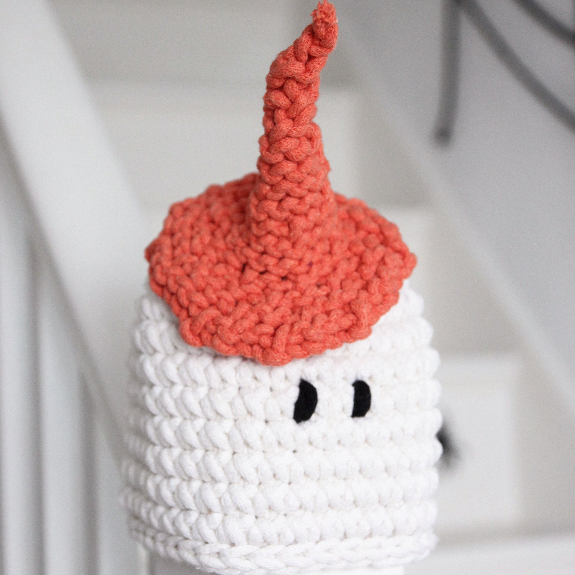 Knitted ghost toy with a red hat on a white background