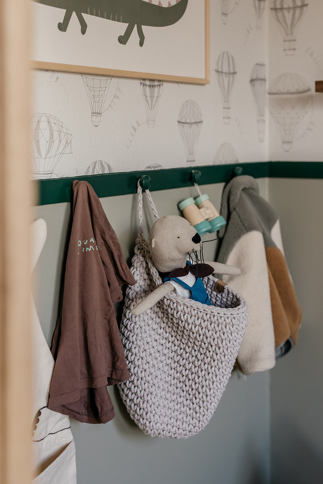 Children's room with hooks on the wall holding clothes and a stuffed animal.