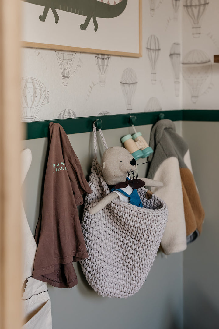 Children's room with hooks on the wall holding clothes and a stuffed animal.