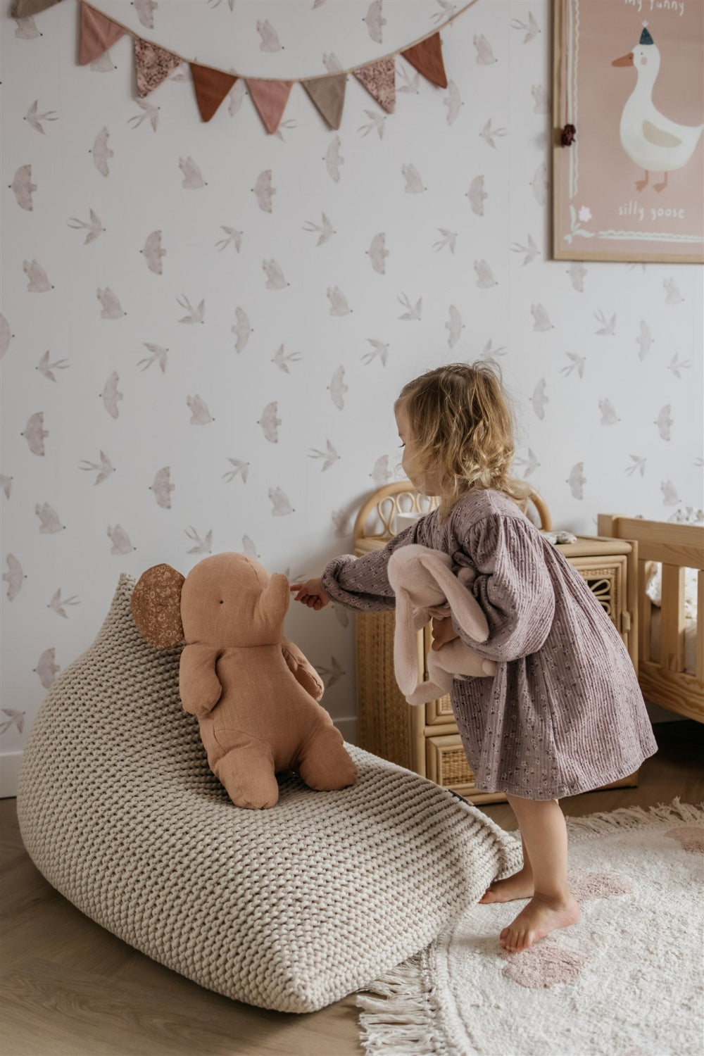 Child playing with a teddy bear in a room with patterned wallpaper and a bean bag chair.