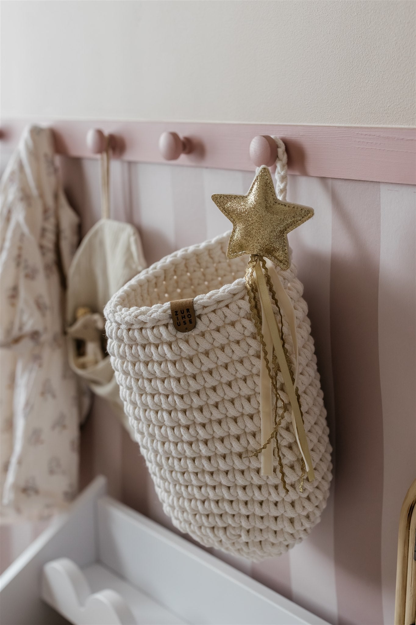 Crocheted basket with a star decoration hanging on a pink wall with hooks.