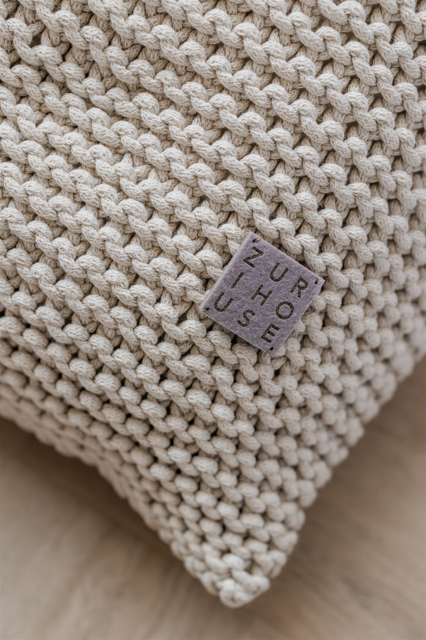 Beige knitted pillow with a visible brand label on a neutral background