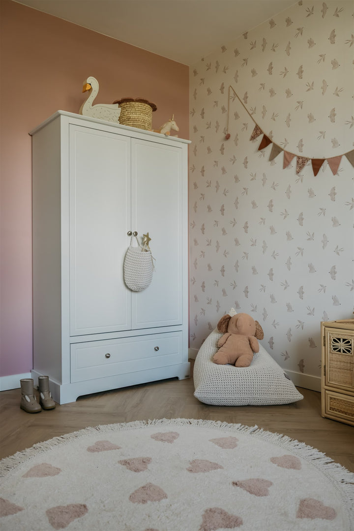 Children's room with a white wardrobe, teddy bear, and decorative items.