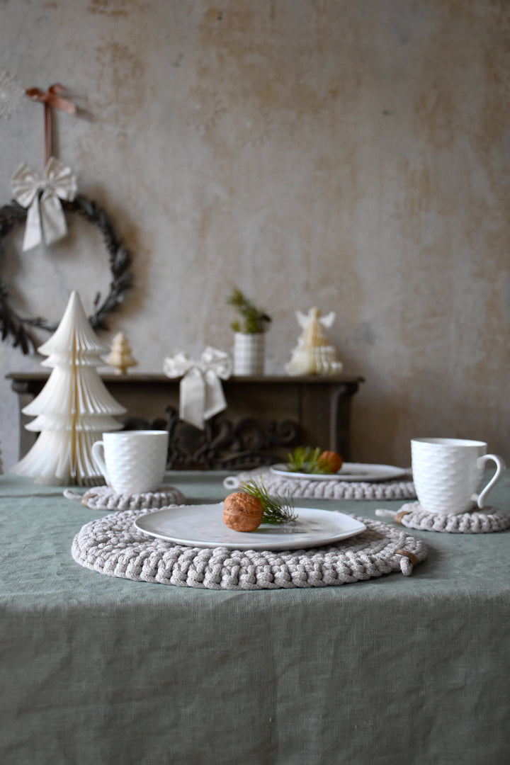 Dining table setting with white crocheted coasters and cups on a textured wall background.