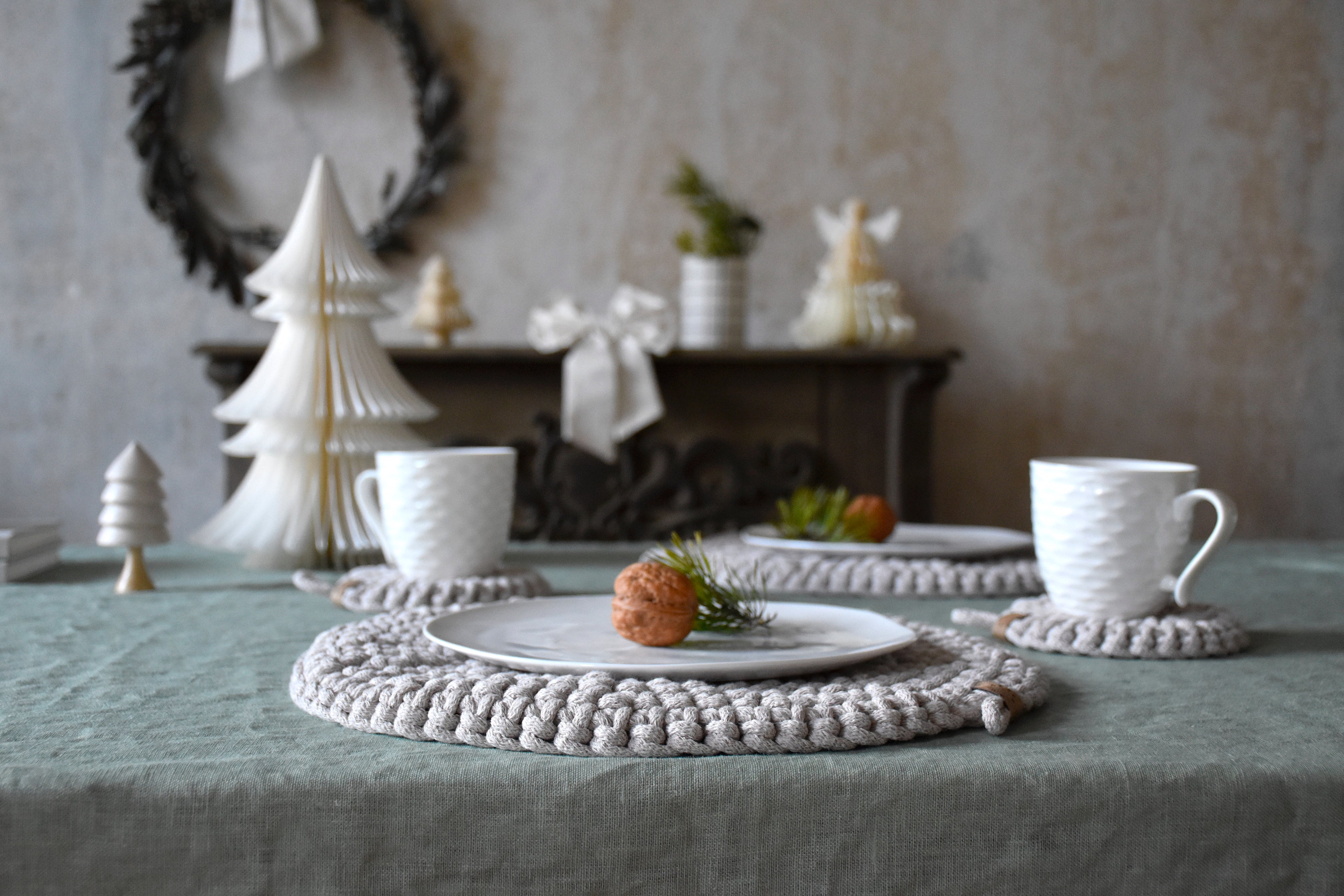 Table setting with white teacups, decorative trees, and a wreath in the background.