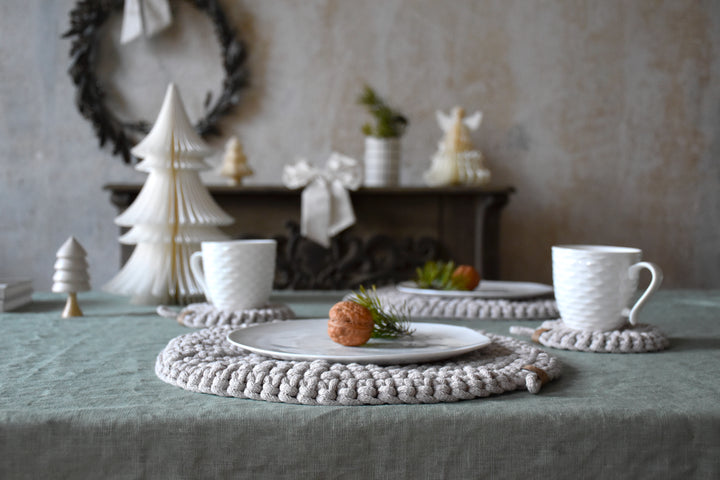 Table setting with white teacups, decorative trees, and a wreath in the background.