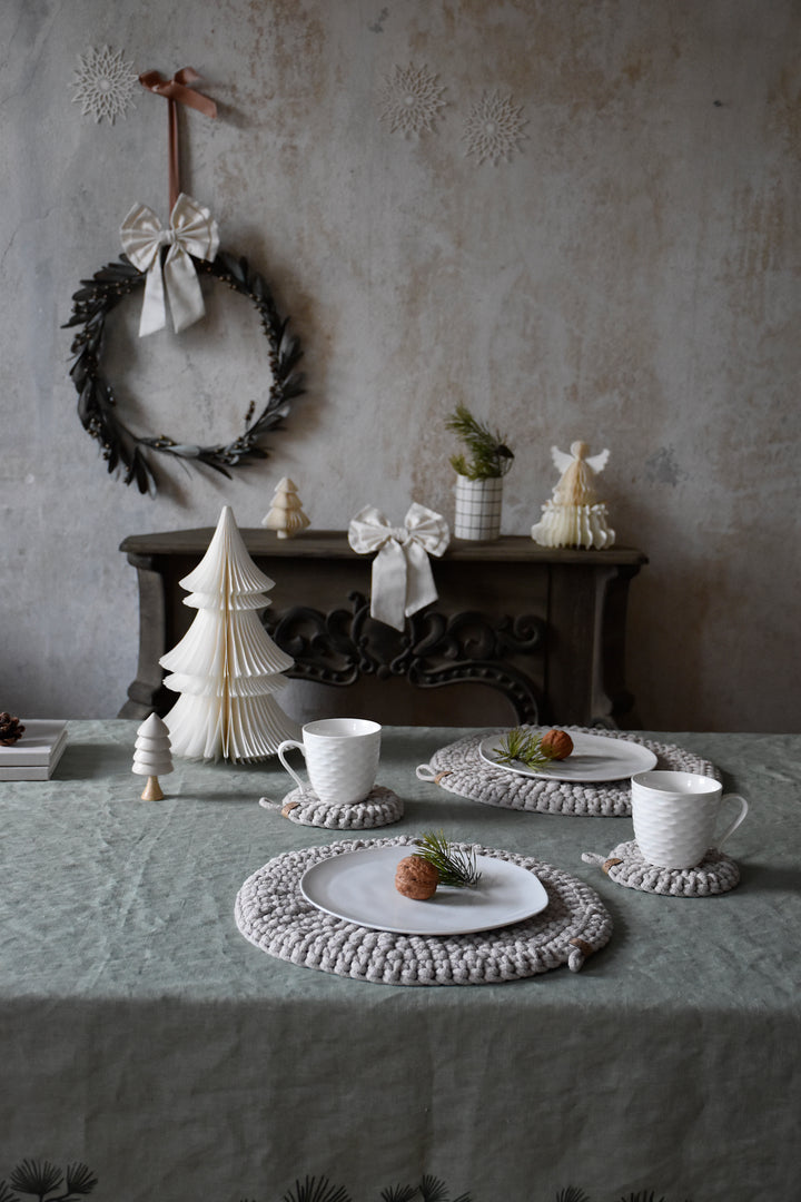 Dining table setting with crocheted placemats, teacups, and decorative items against a textured wall.