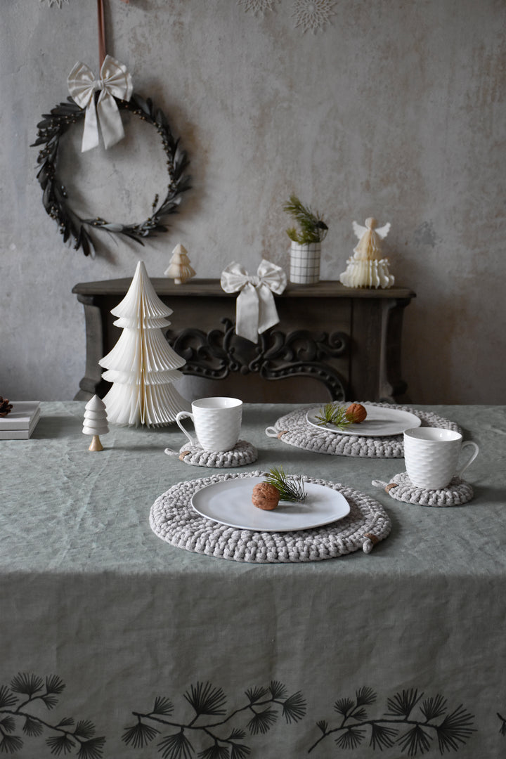 Decorative table setting with Christmas trees, cups, and a wreath on a textured wall.