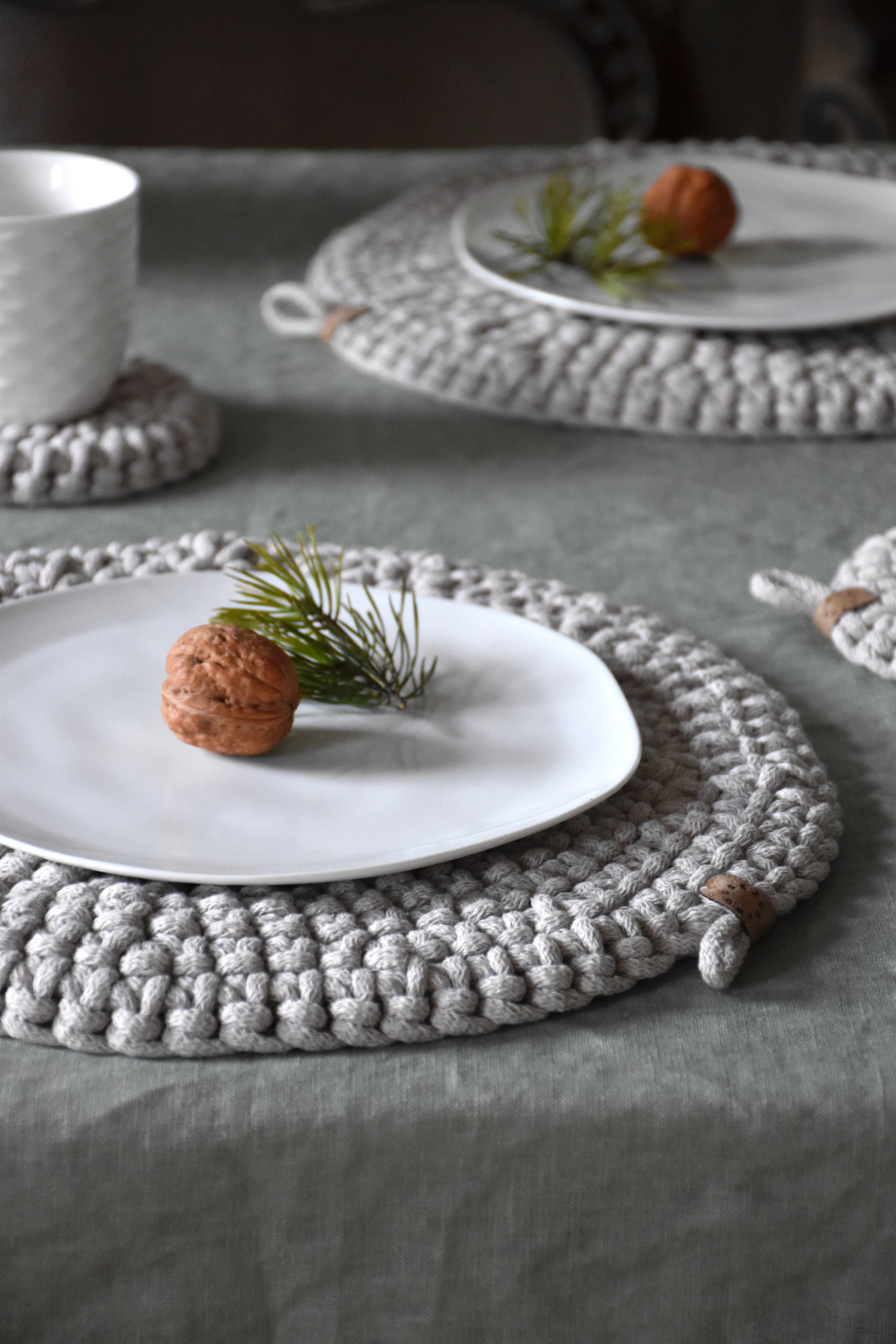 Table setting with white plates and woven placemats on a gray tablecloth.
