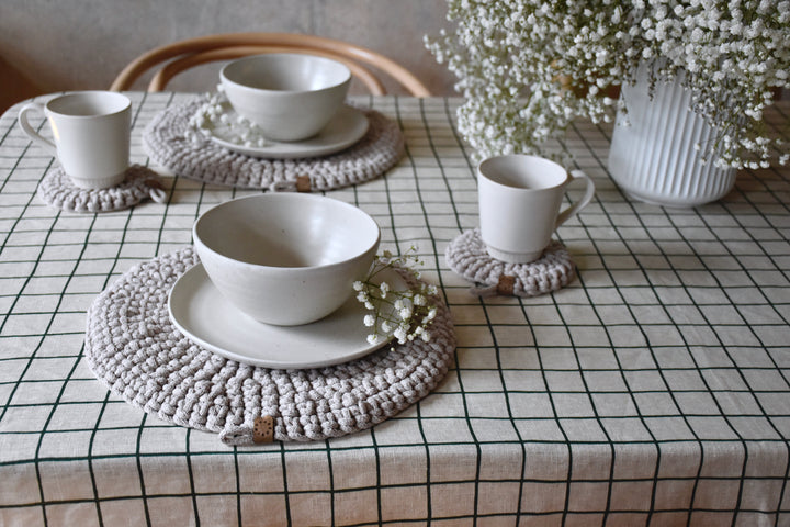 White ceramic bowls and cups on textured placemats with a checkered tablecloth and decorative elements.