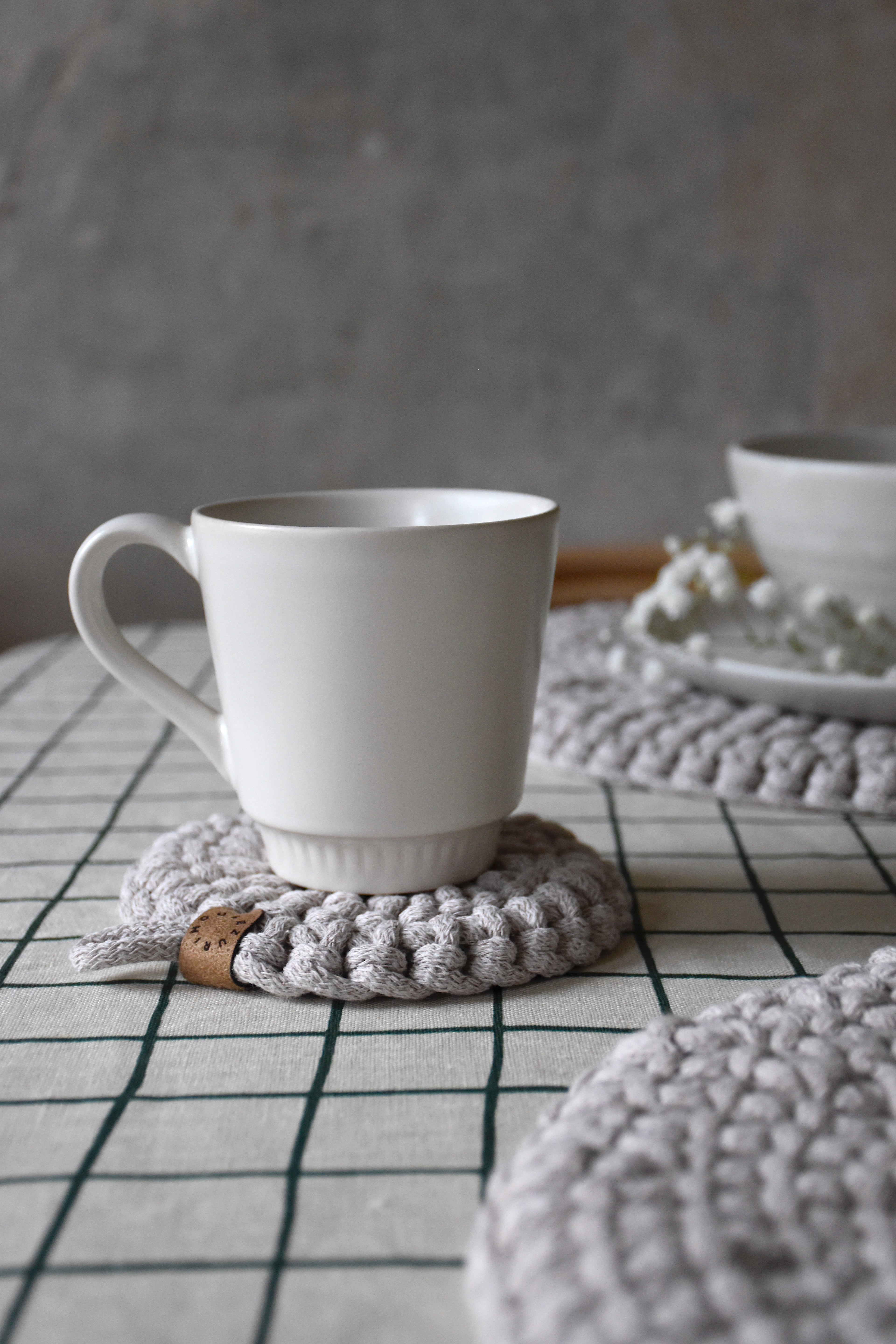 White mug on a textured gray coaster with a blurred background