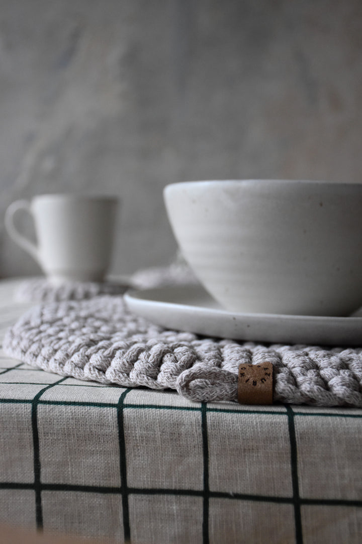 White ceramic bowl and mug on a textured surface with a woven trivet.