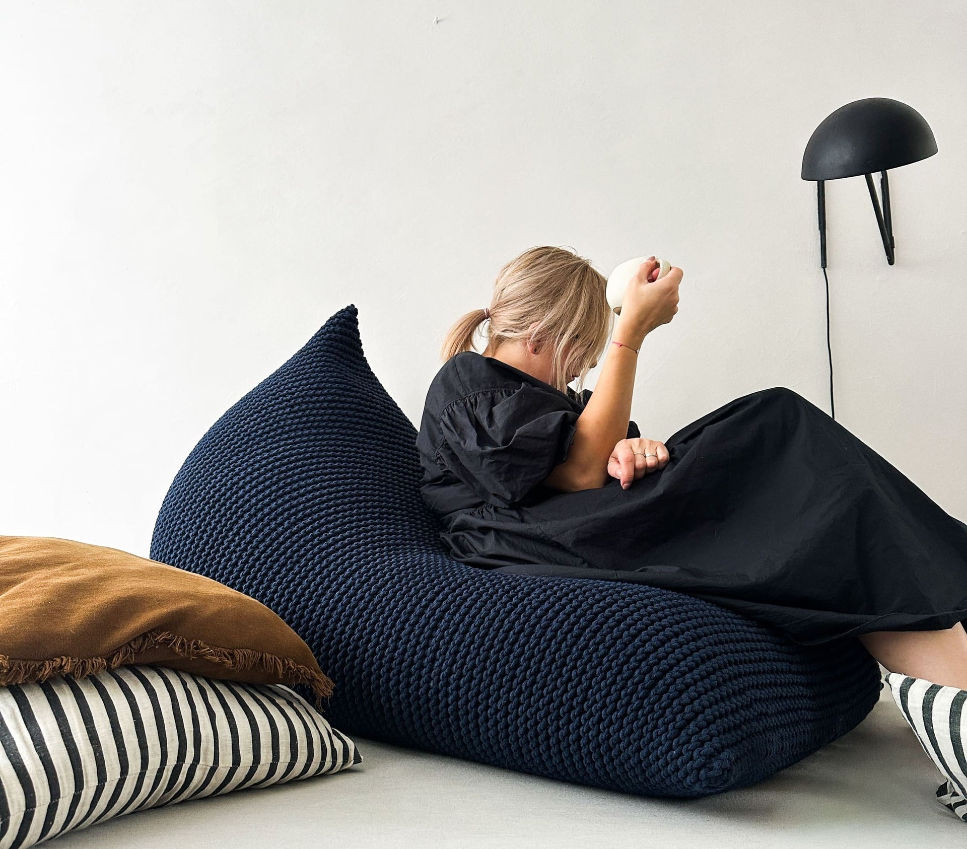 a girl sitting on a navy blue knitted bean bag chair and drinking coffee