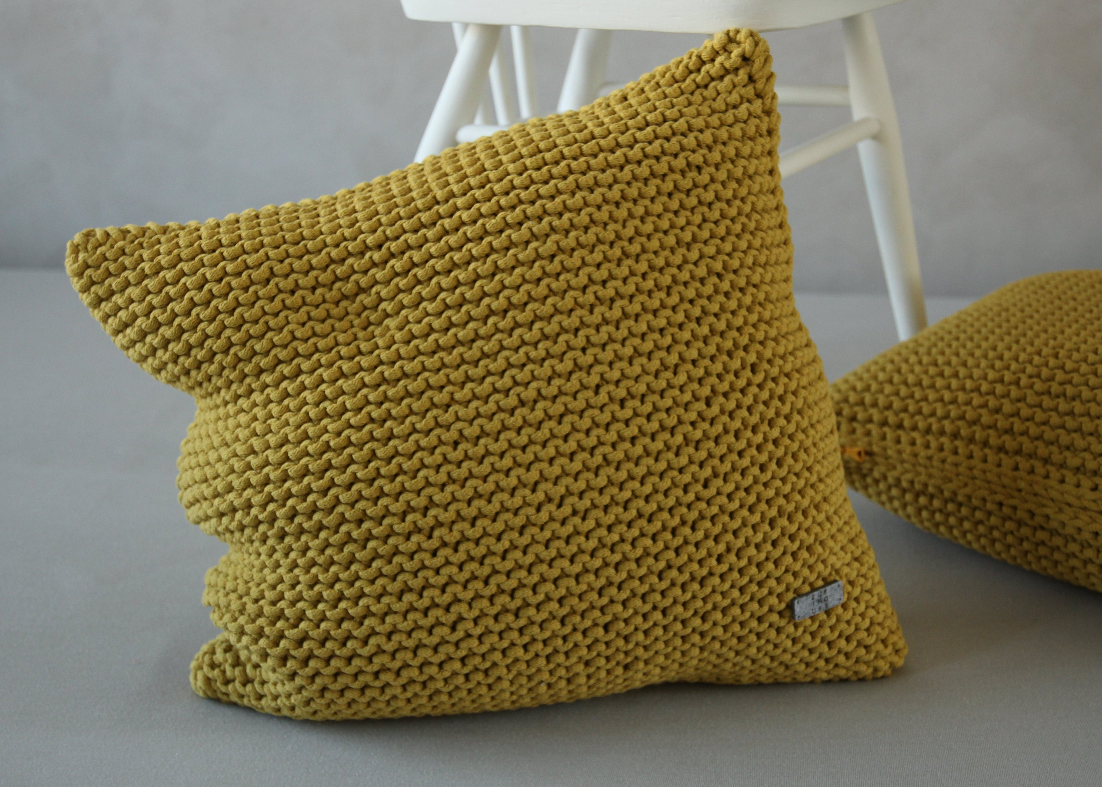 Knitted yellow cushions on a gray surface with a white chair in the background.