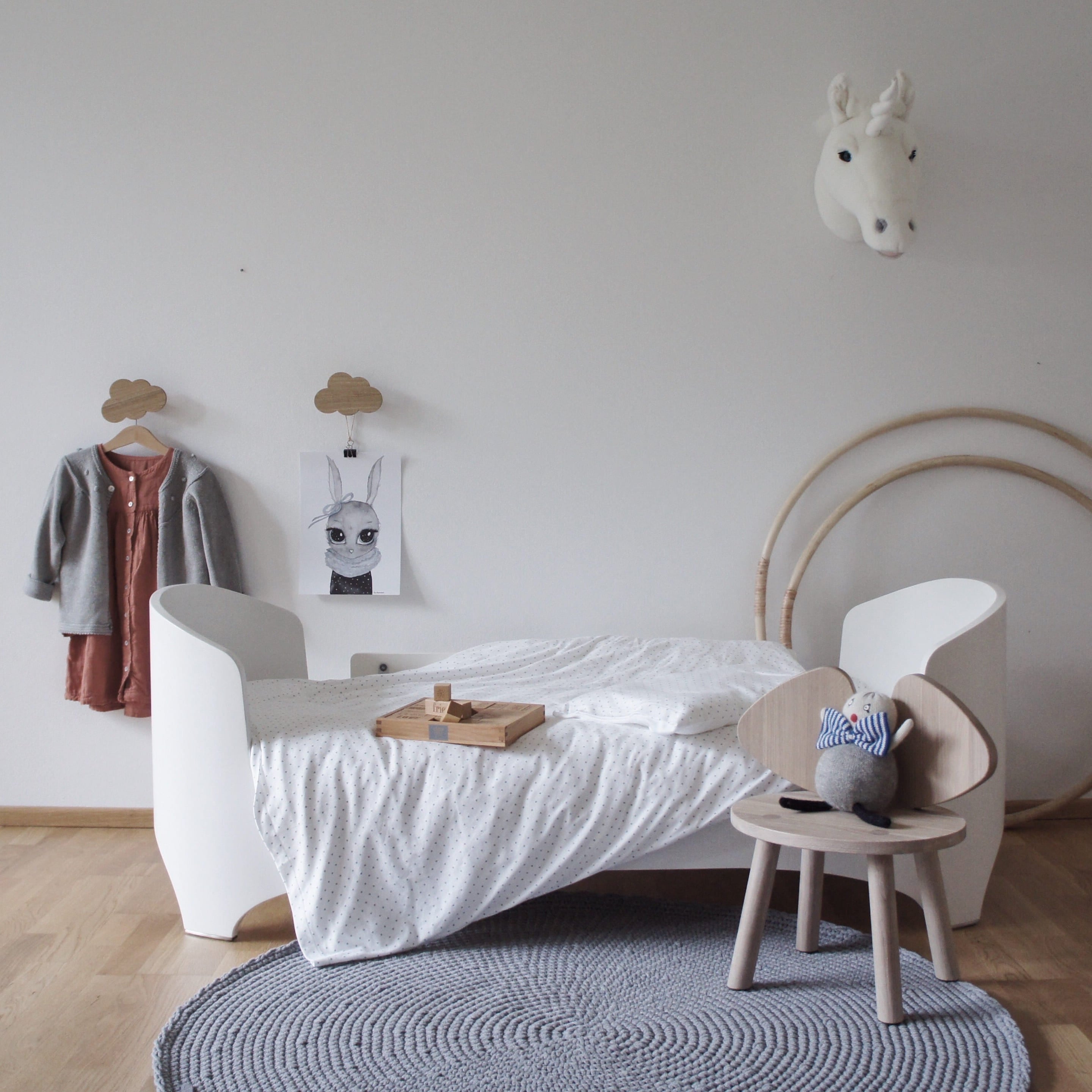 Children's bedroom with white bed, wooden chair, and decorative items on a light gray wall.