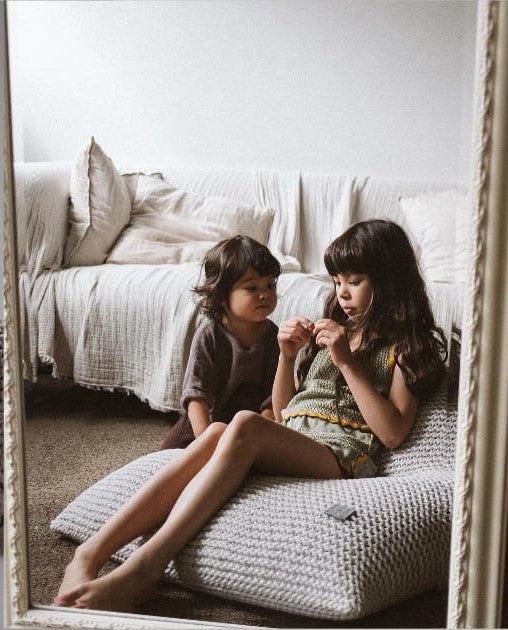 Two children sitting on a textured bean bag chair with a mirror reflecting their image.