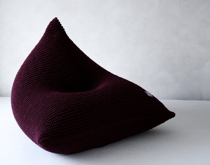 Hand-knitted bean bag in deep aubergine yarn in a neutral studio setting