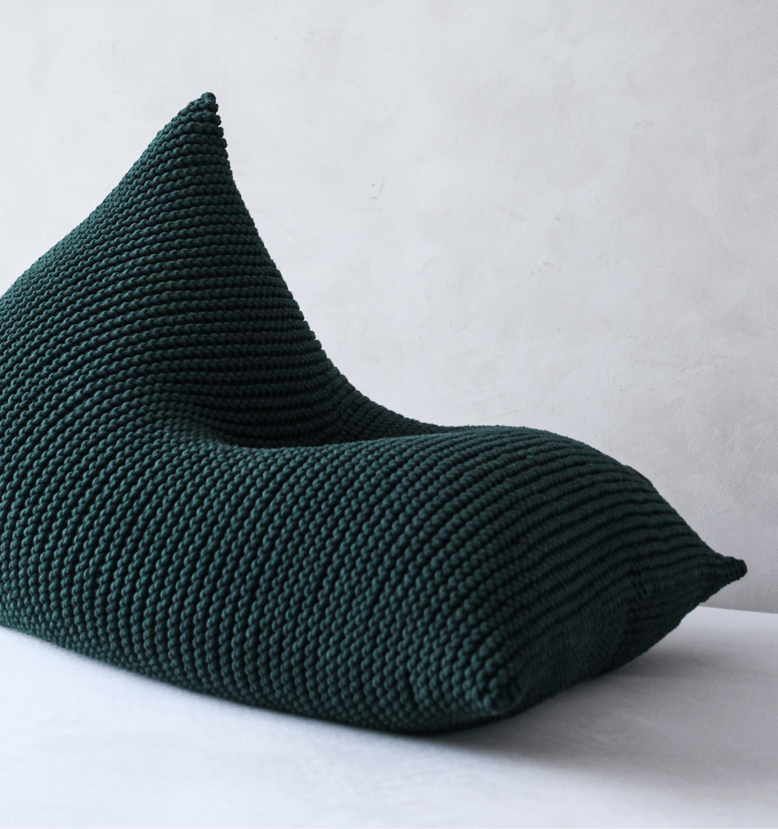 Hand-knitted bean bag in deep bottle green yarn photographed in a minimal setting