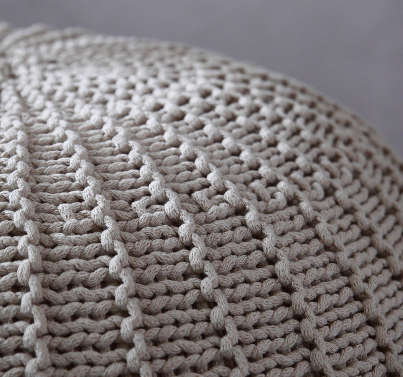Close-up of a chunky knit textile in a warm light taupe-beige color, showing the detailed knit pattern and soft texture.