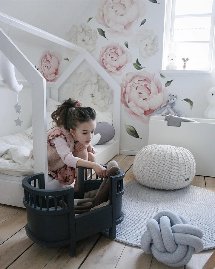 Children playing in a playhouse with floral wallpaper and soft decor in a child's room.