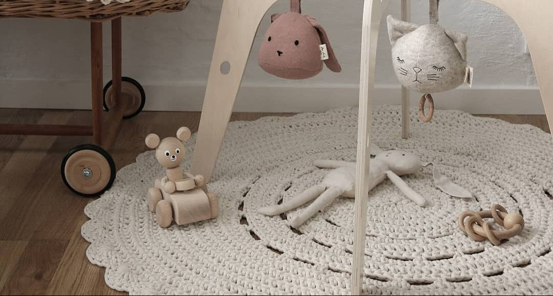 Nursery with wooden baby gym, toys, and wicker crib on the crochet ecru rug