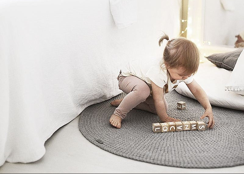 Child playing with blocks on a gray rug in a bedroom