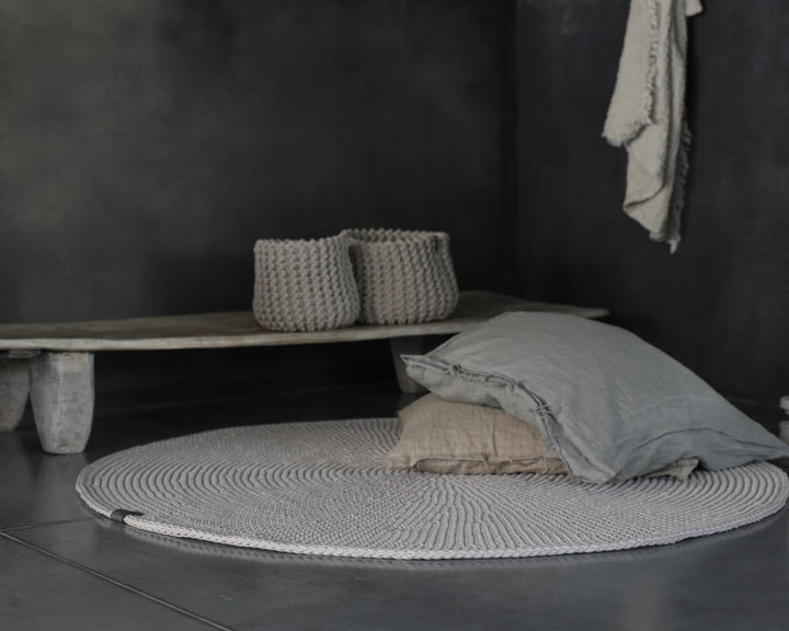 Round woven rug with pillows and baskets in a minimalistic room.