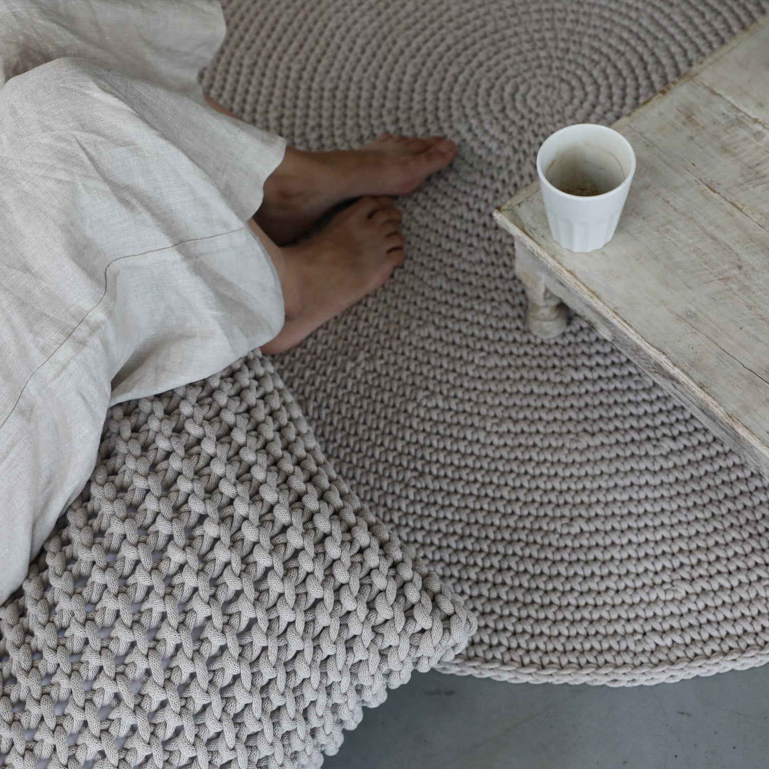 Person lying on a textured rug with a cup on a wooden table nearby