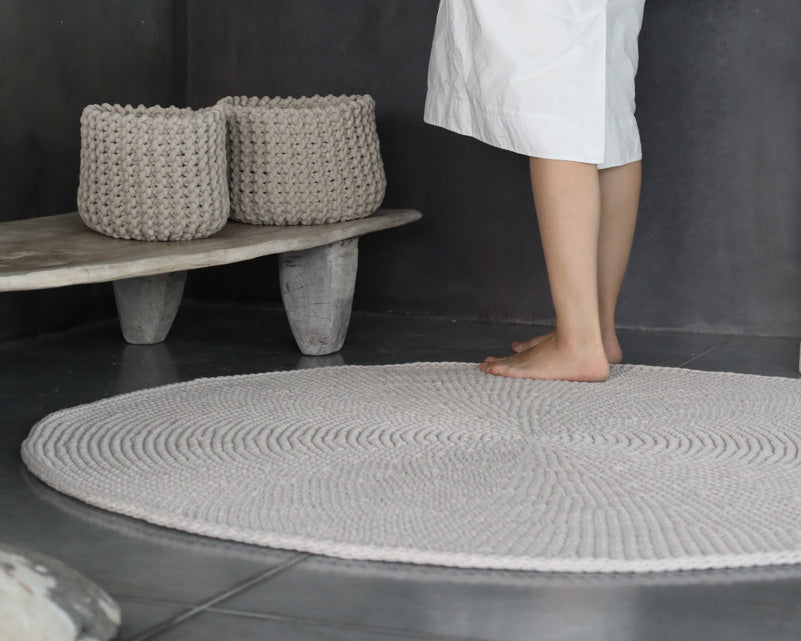 Person standing on a textured gray bath mat in a bathroom setting with woven baskets in the background.