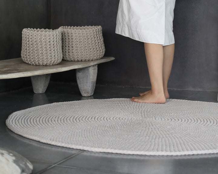Person standing on a textured gray bath mat in a bathroom setting with woven baskets in the background.