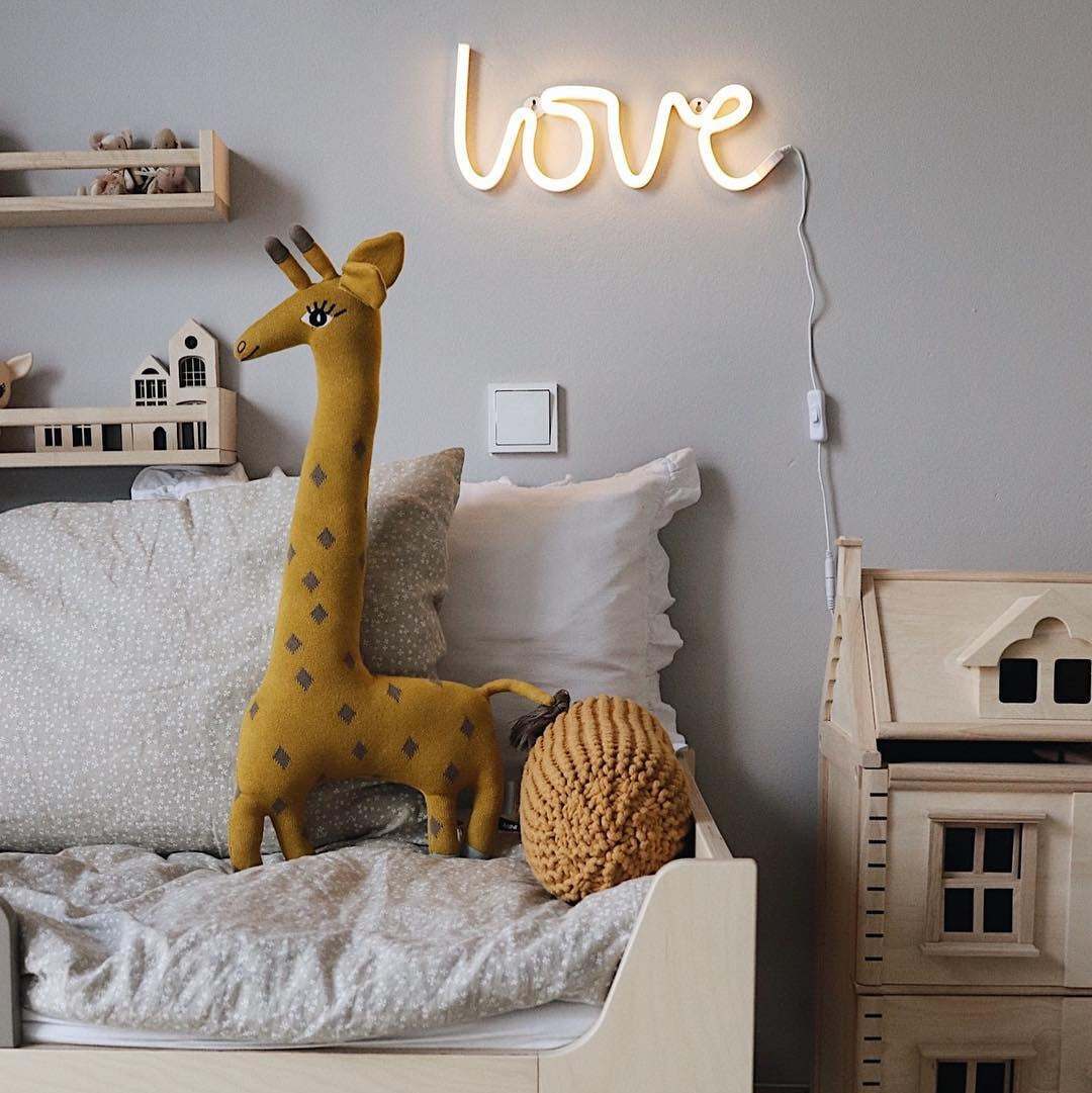 Children's bedroom with a bed, plush toys, and a neon 'love' sign on the wall.
