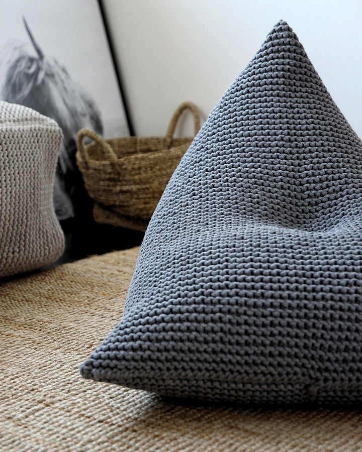 Tactile surface of a dark grey hand-knitted bean bag in a clean, empty space
